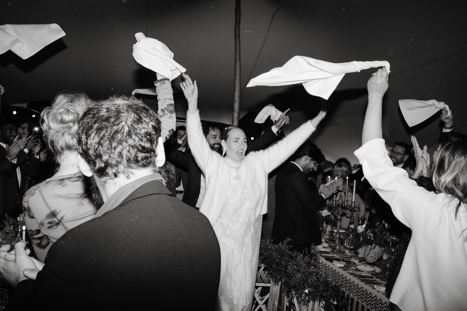 Wedding guests waving white napkins in celebration during a festive reception.