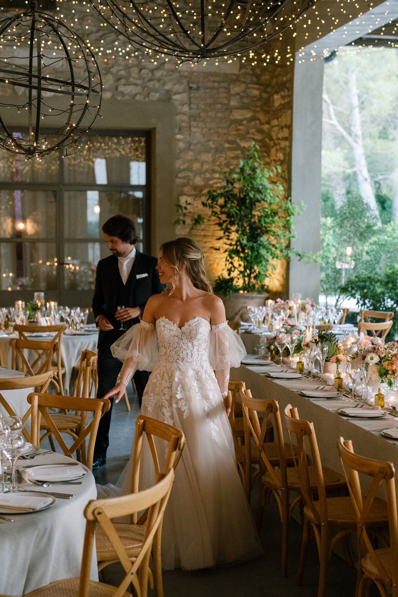 Wedding reception venue with string lights, wooden chairs, and elegant table settings.
