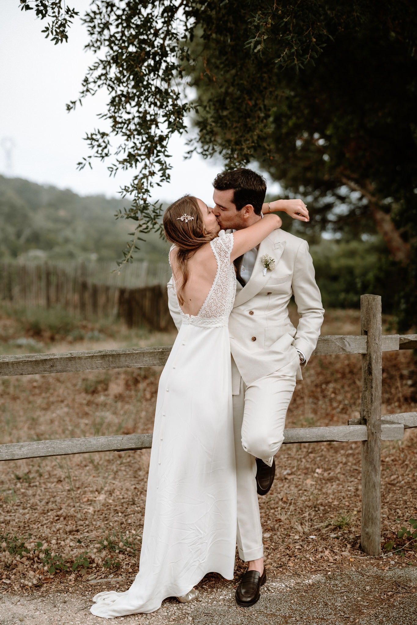 A romantic wedding couple shares an intimate moment against a rustic wooden fence backdrop.
