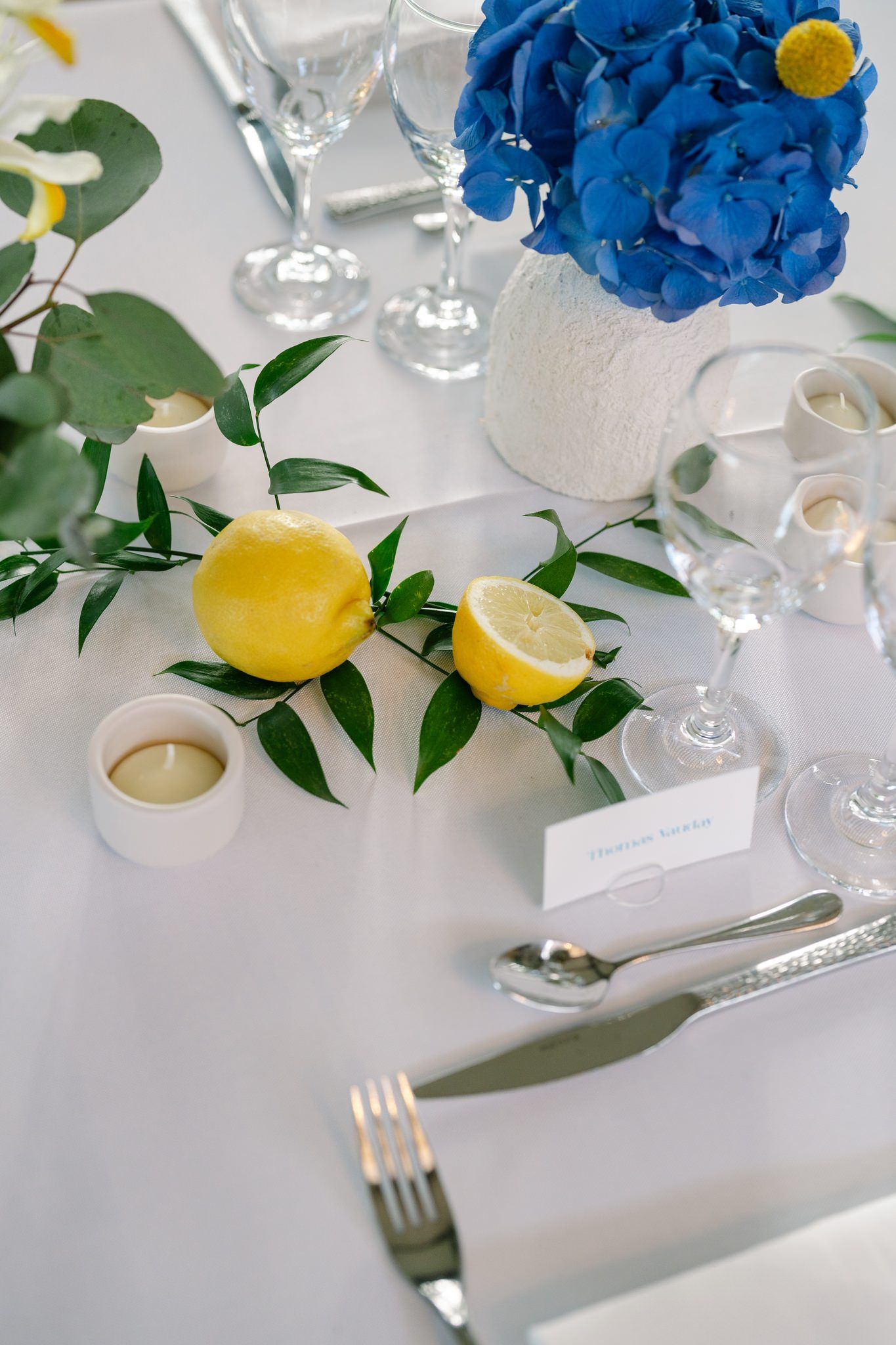Modern table setting with bright blue hydrangeas, lemons and white linens.
