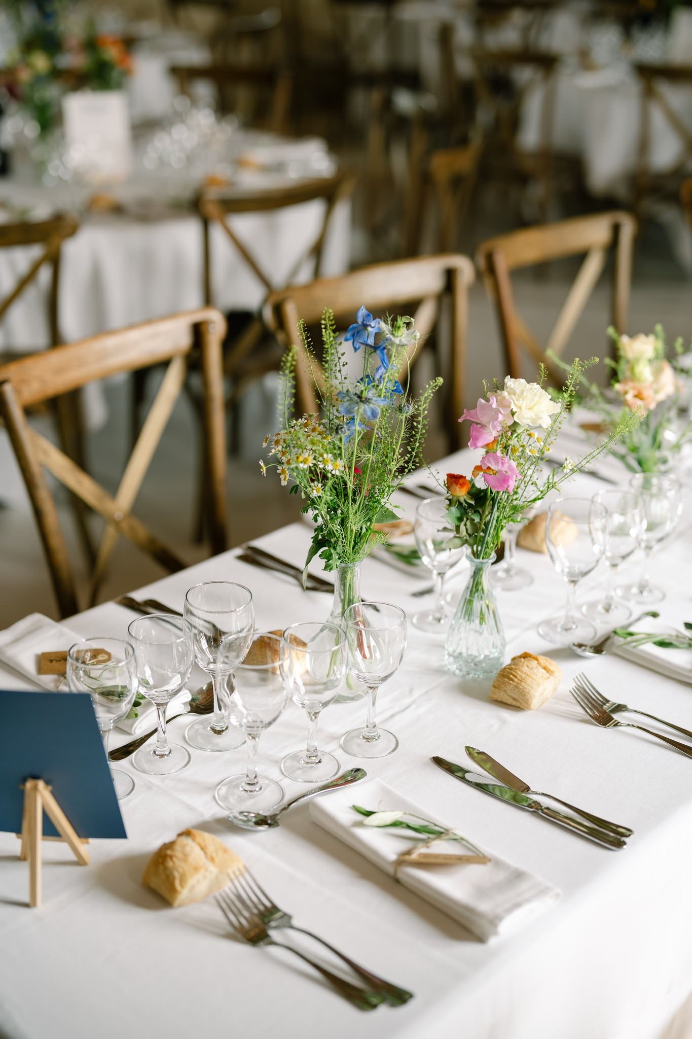 Elegant wedding table settings with rustic wooden chairs and fresh floral centerpieces.