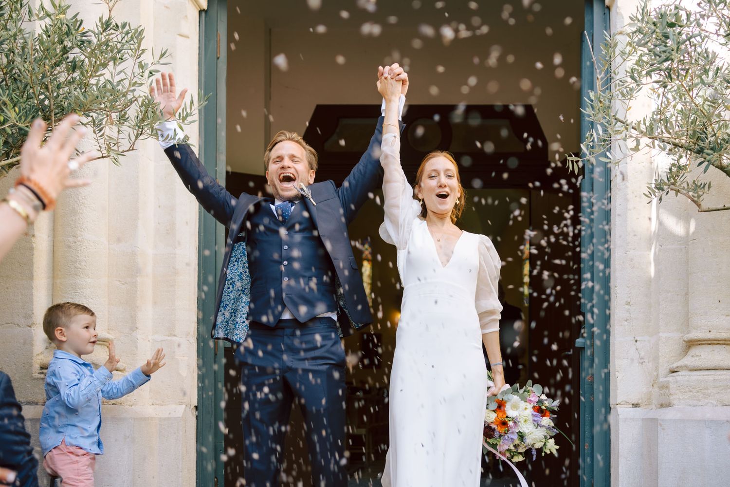 Joyful wedding celebration with guests throwing confetti outside church entrance.
