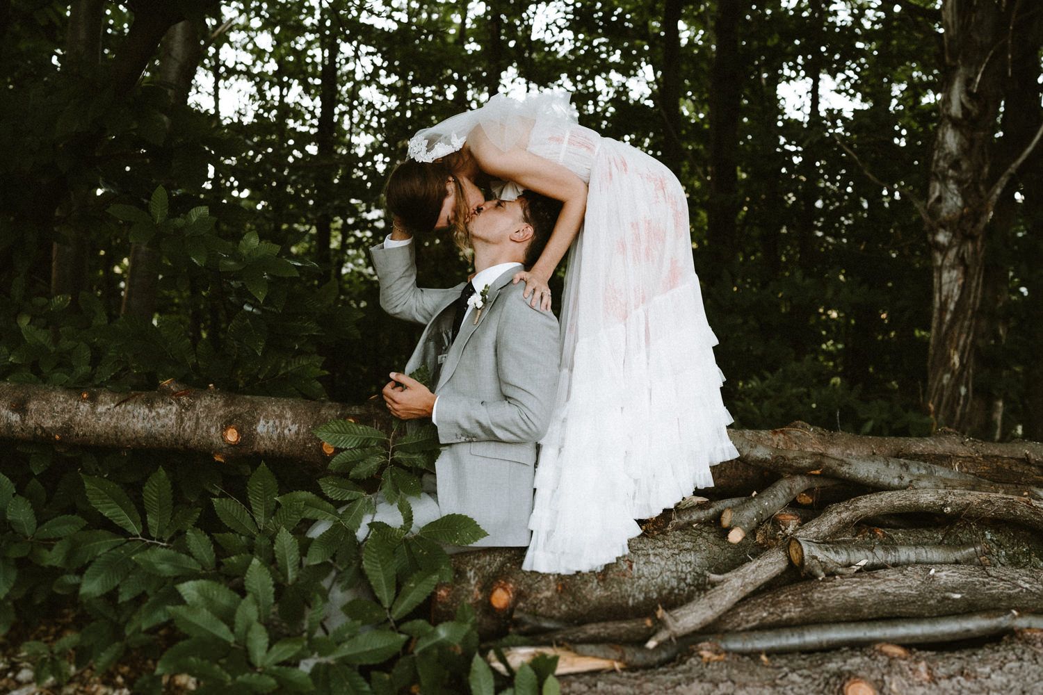 Artistic wedding photo of couple embracing on rustic wooden logs in a forest setting.
