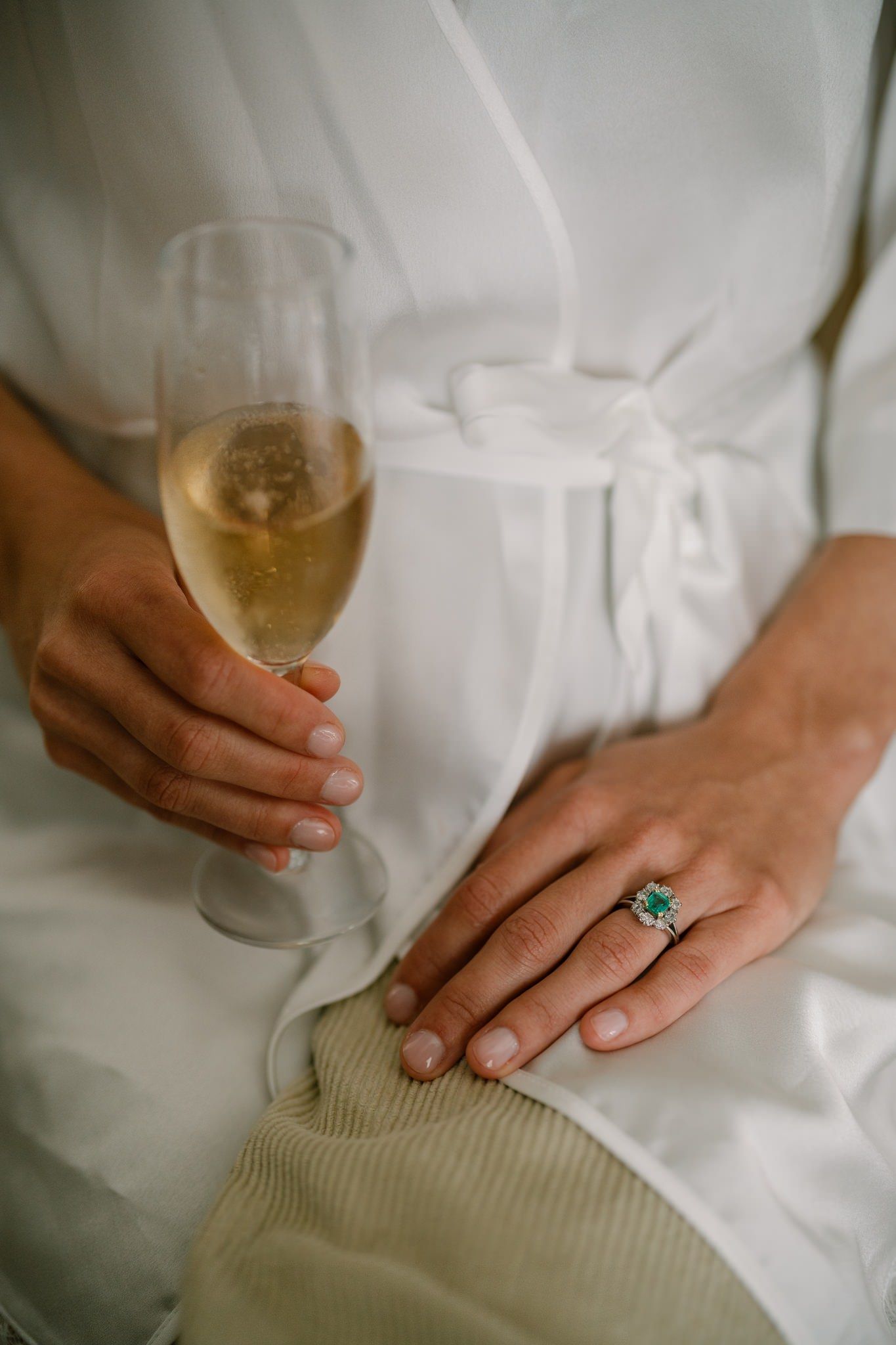 Close-up of hands holding a champagne glass and wearing an engagement ring against a white dress.