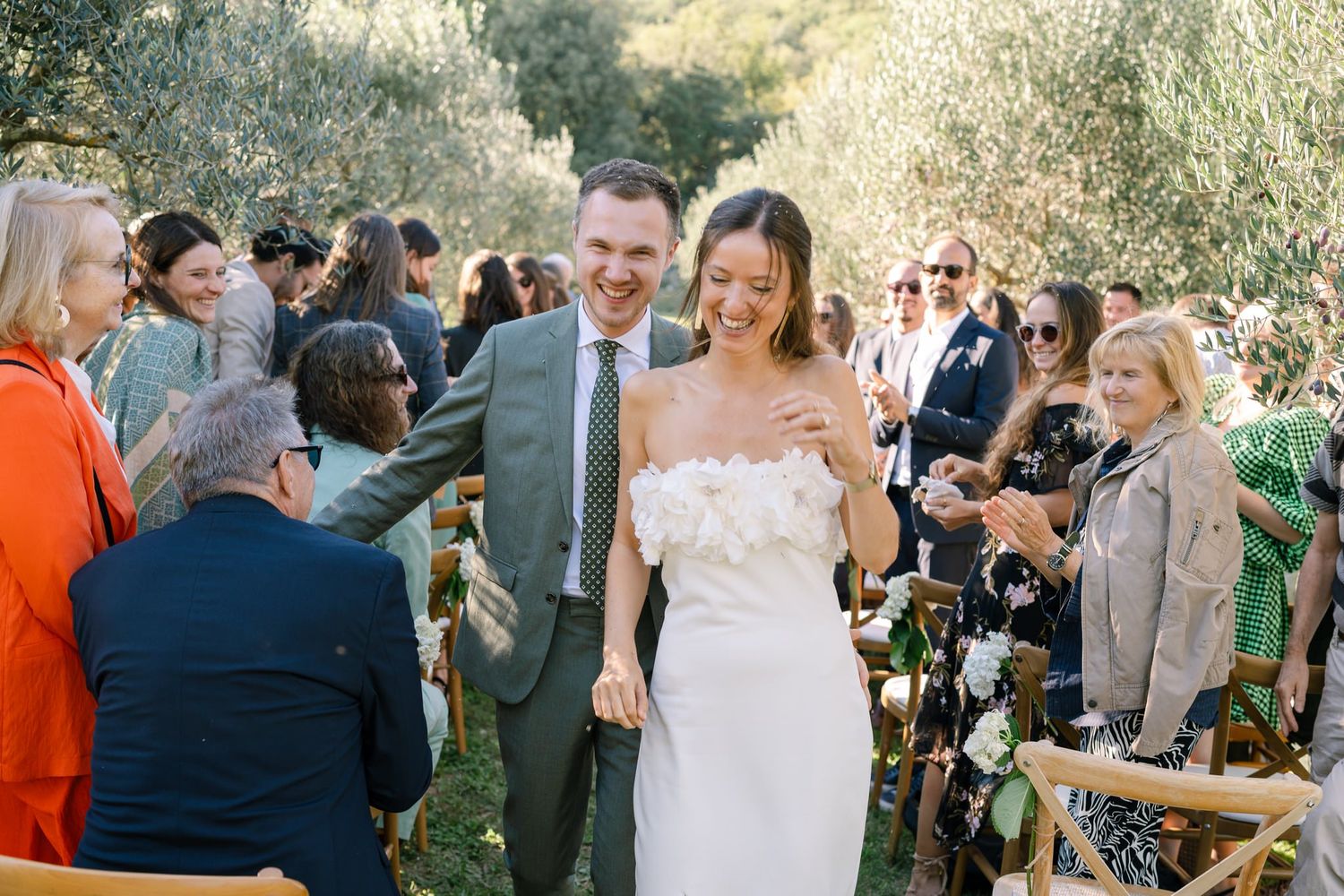 Wedding guests celebrate during an outdoor reception beneath olive trees with string lights.