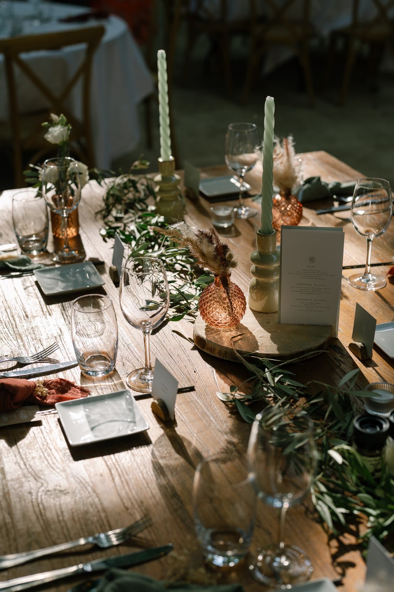 Rustic wedding reception table with candles, greenery, and place settings on a wooden surface.