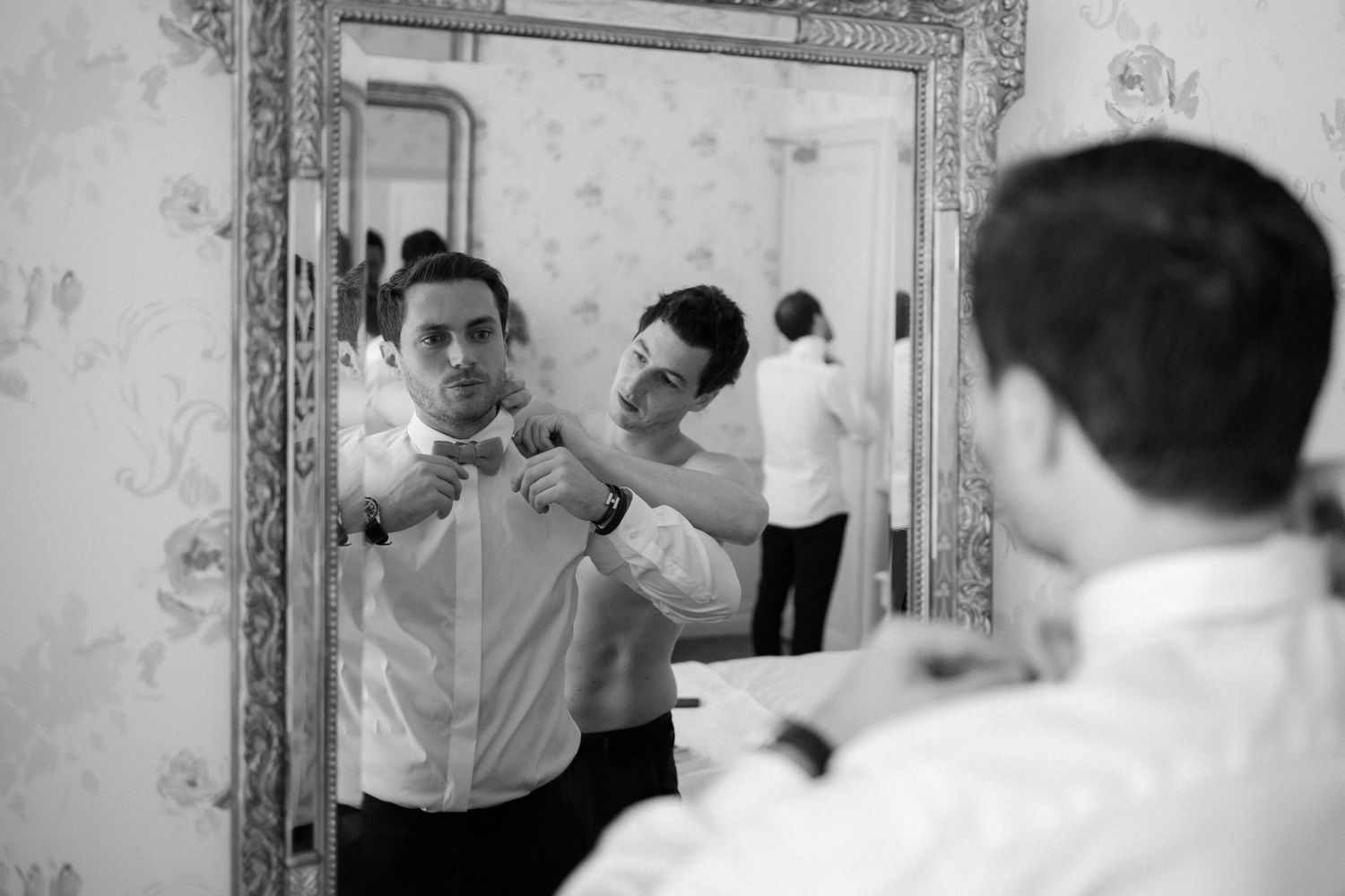 Black and white image of formal preparation in front of ornate mirror.