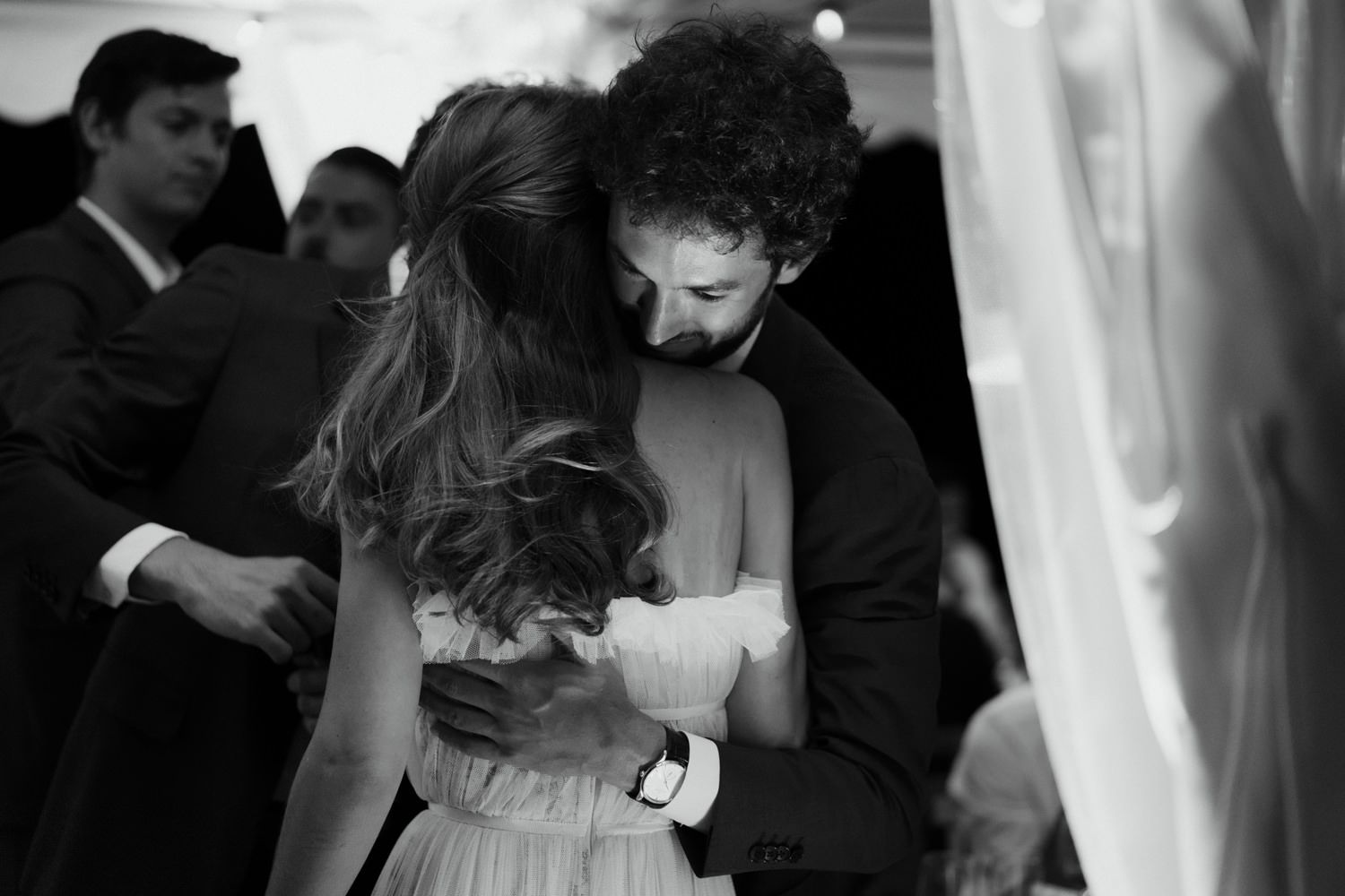 Wedding guests dancing and embracing on a dimly lit dance floor during a celebration.