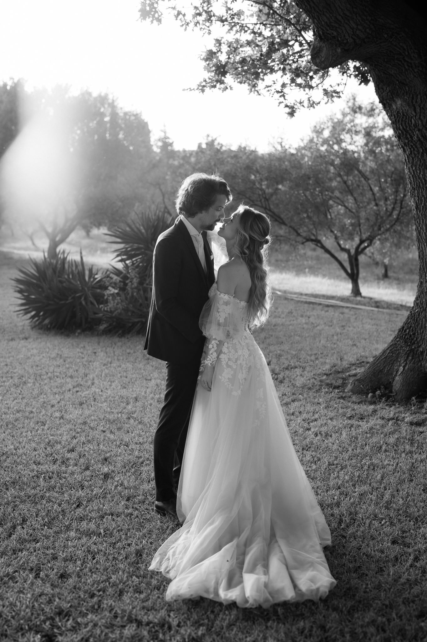 Romantic black and white portrait of a couple in wedding attire under a tree.