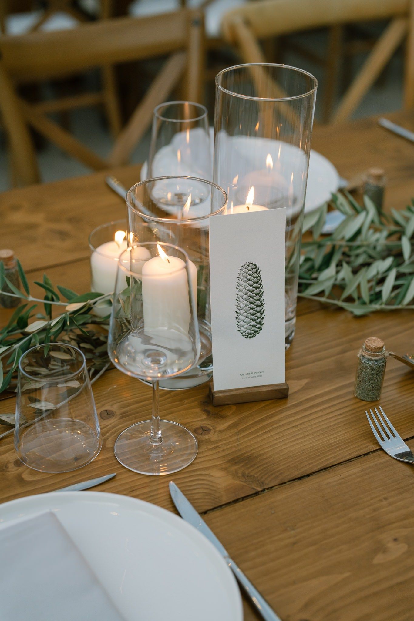 Wedding table decor featuring pinecone place cards, candles, and olive branches on rustic wood tables.