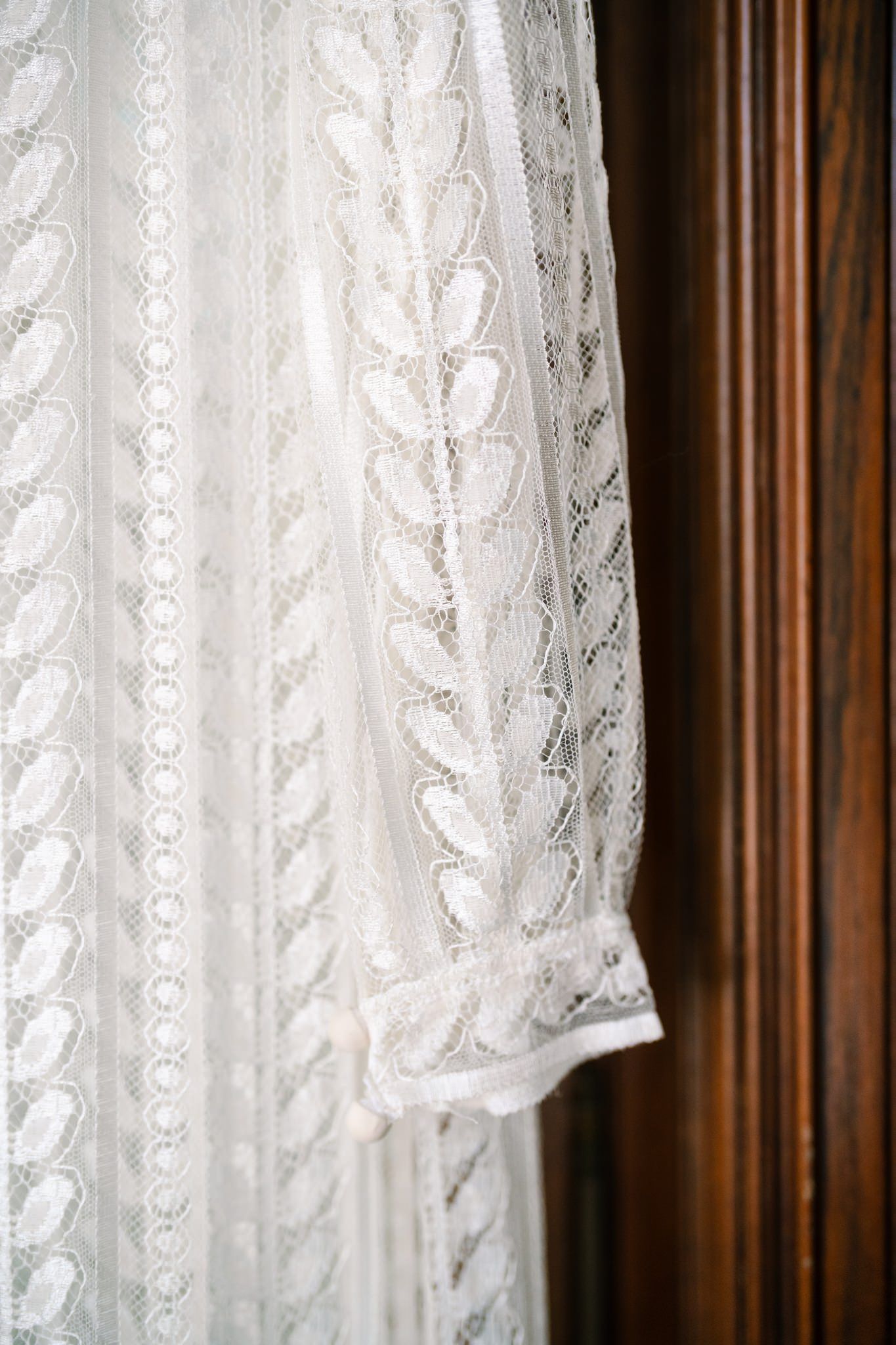 Delicate white lace curtains hanging against dark wooden window trim.
