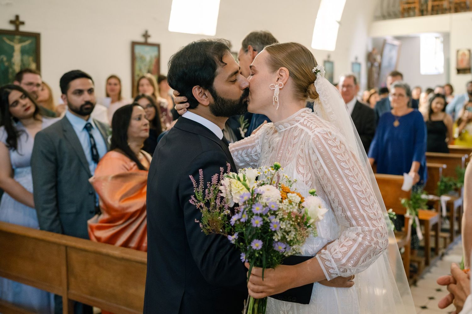 Wedding ceremony guests mingle and embrace in a church setting with warm lighting and floral decorations.