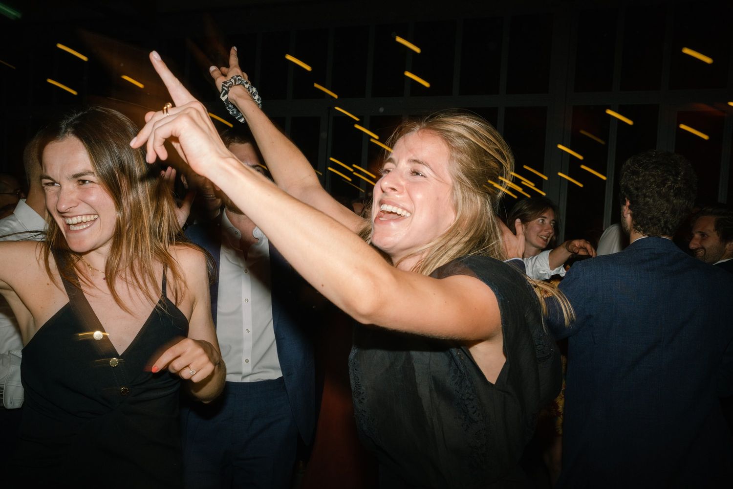 Wedding guests dance energetically on a dark dance floor with sparklers creating light trails above.