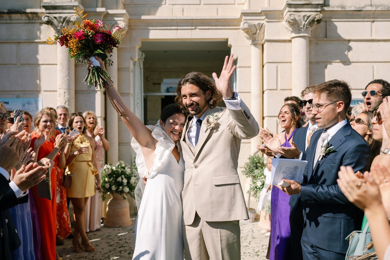 Joyful wedding celebration with guests cheering outside a classic stone building entrance.