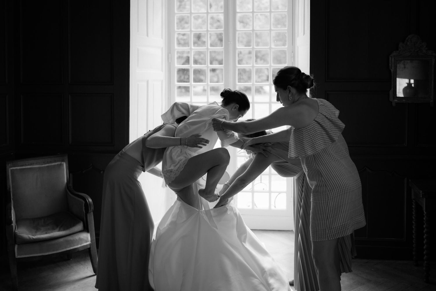 Silhouettes against bright window light in a dark room during wedding preparations.
