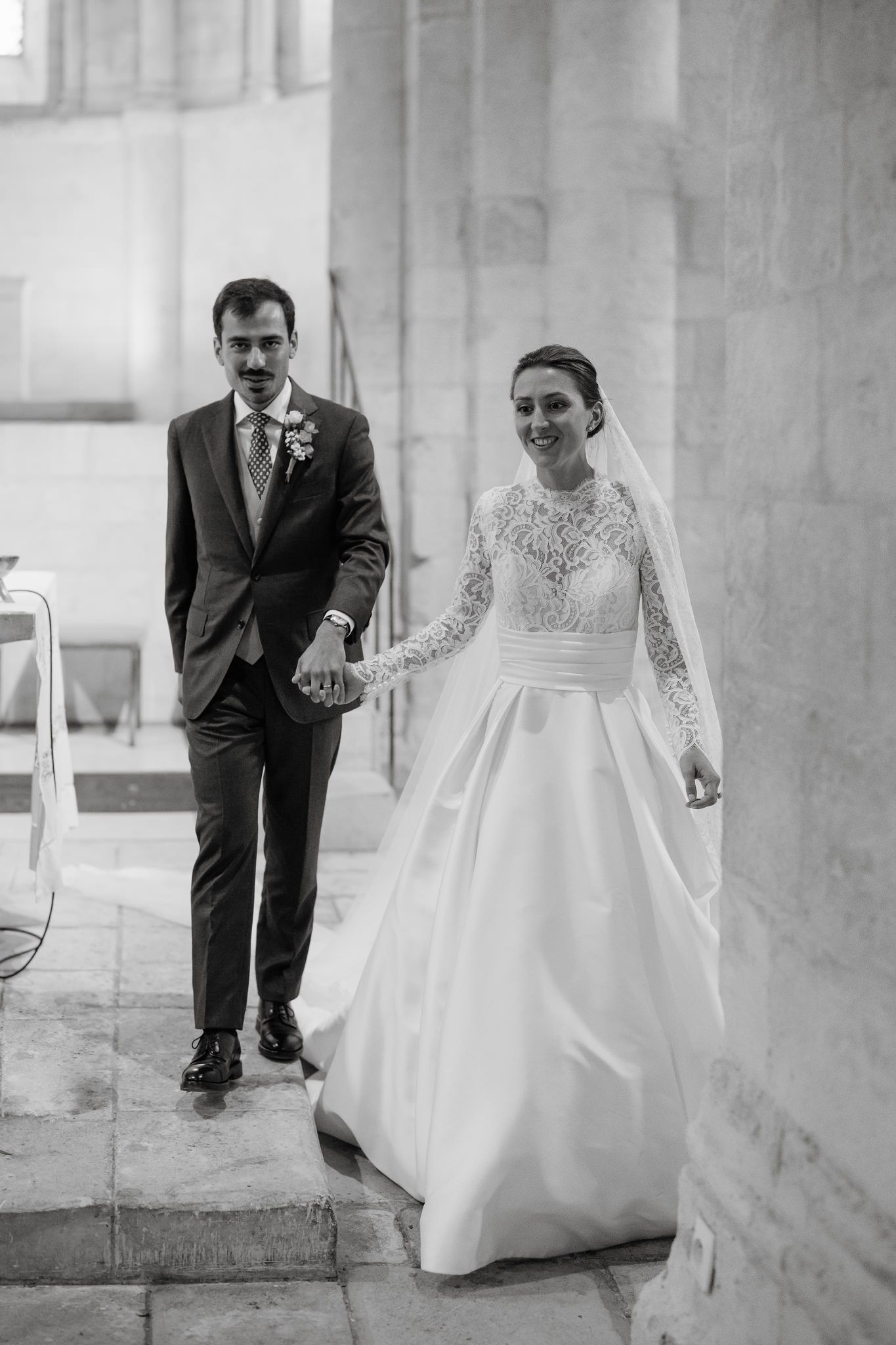 Wedding couple walking through a stone hallway with elegant architectural details.