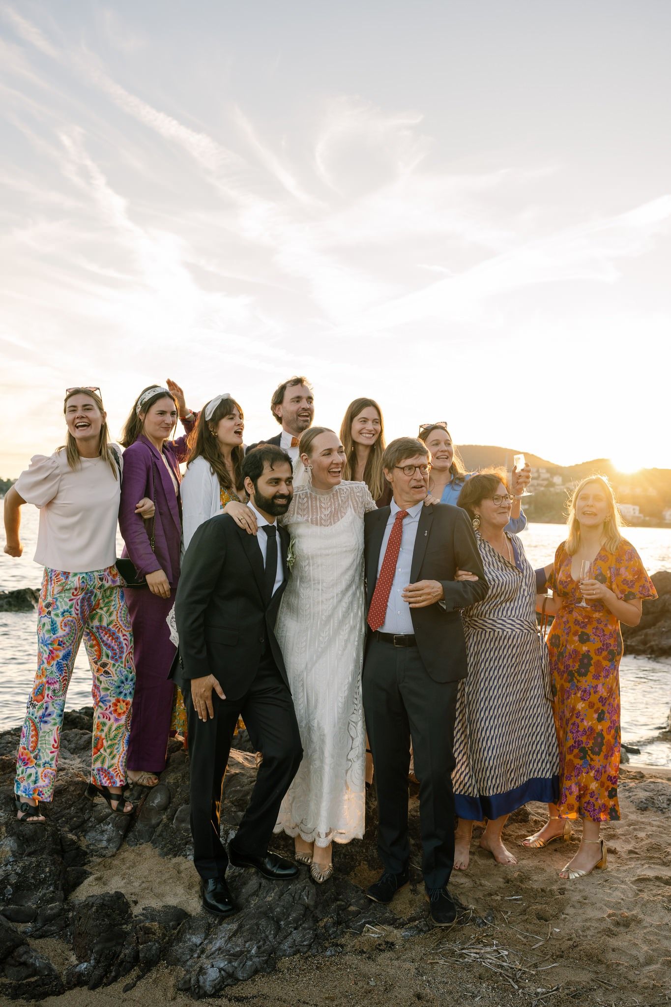 Wedding party poses together on beach at sunset with ocean in background.