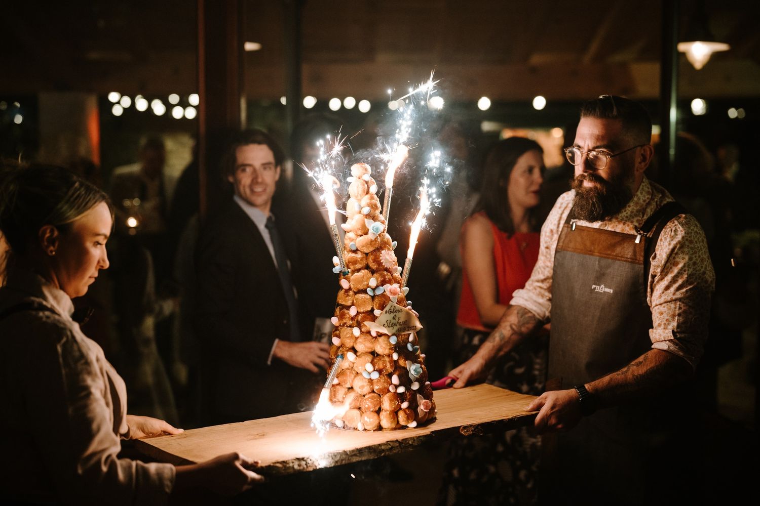 Sparklers illuminate a dark wedding reception as guests celebrate.