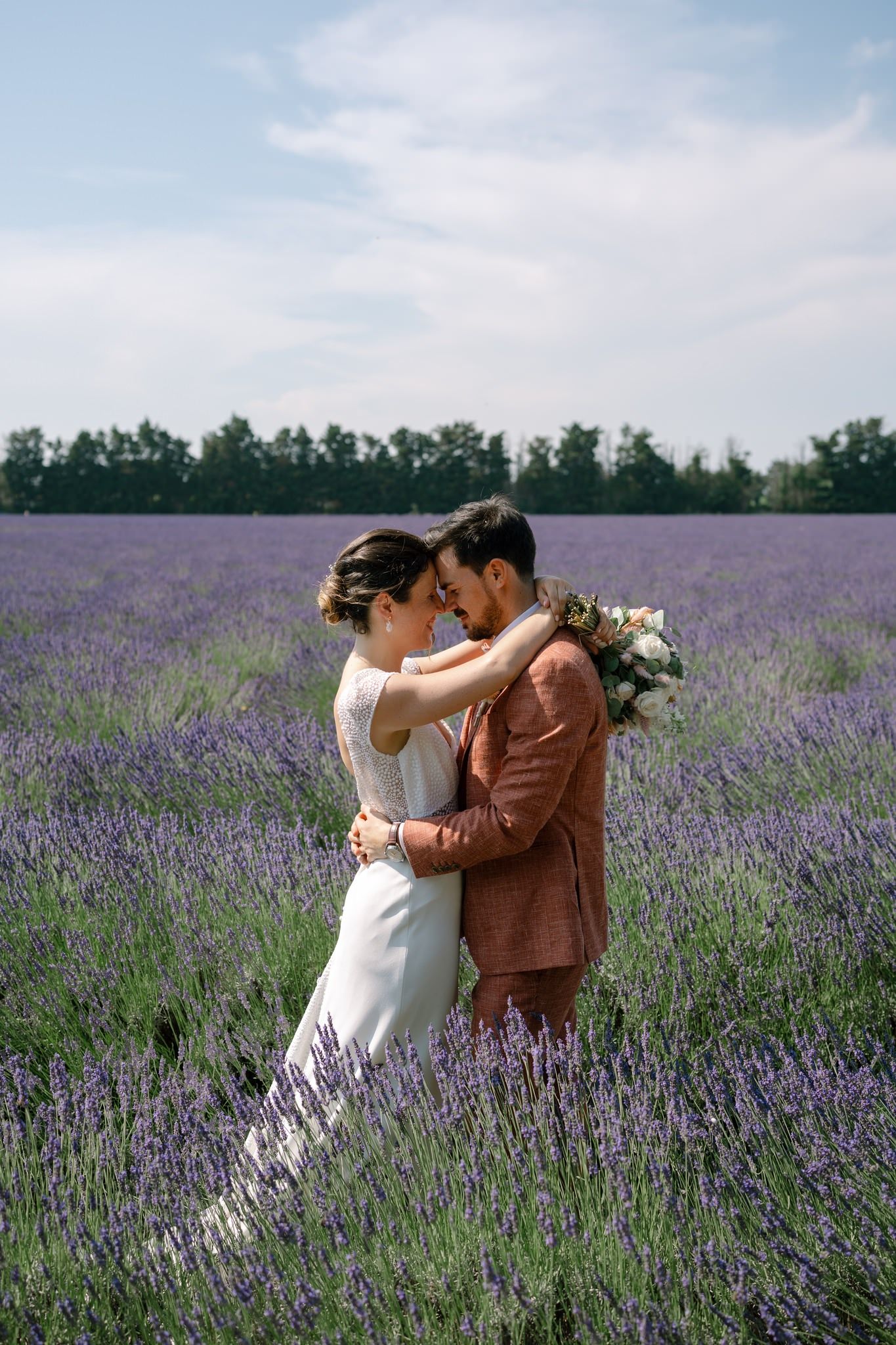 Couple embracing in a blooming lavender field on their wedding day.
