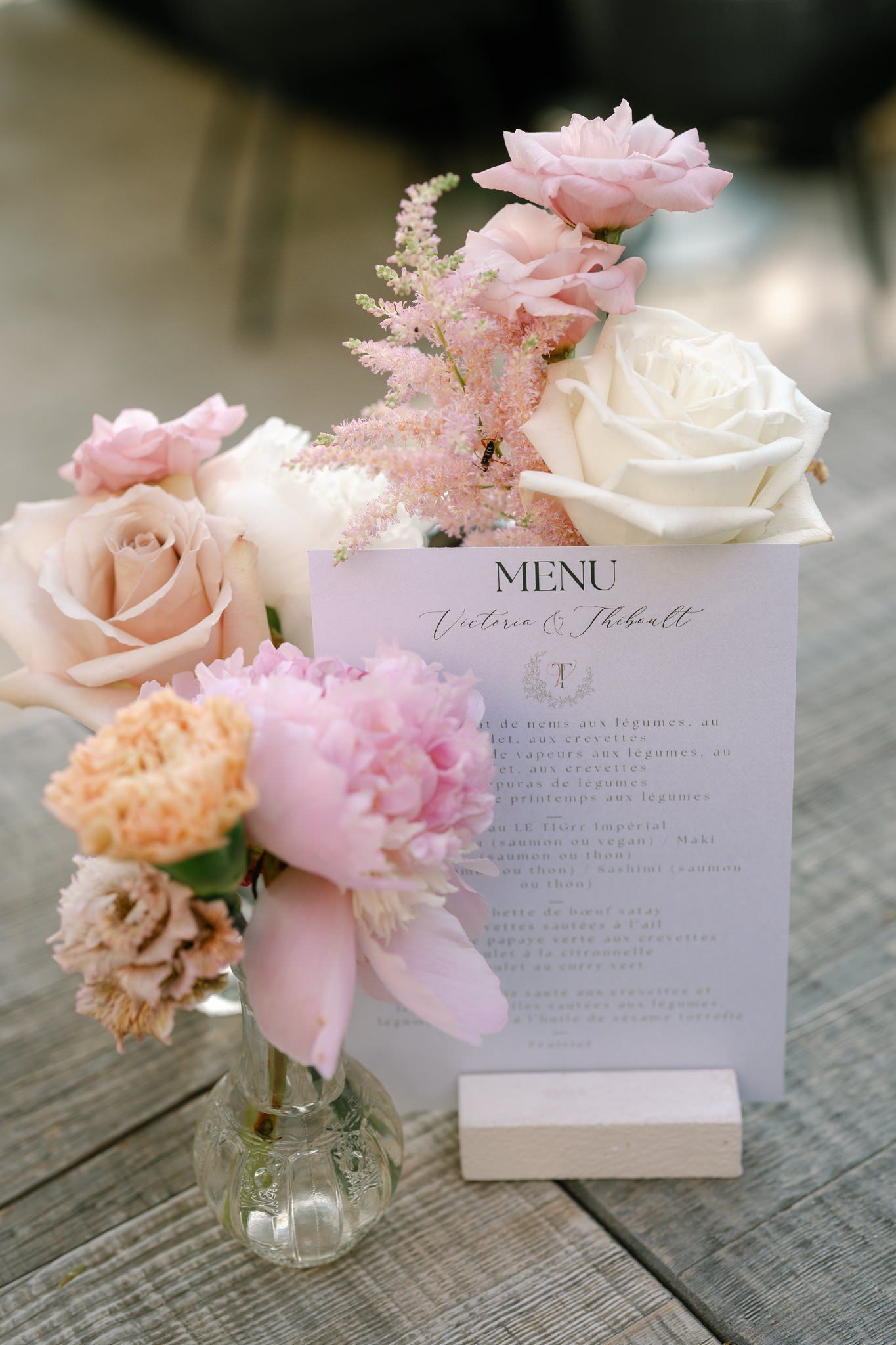 Delicate pink and white floral arrangements with menu cards on a rustic wooden surface.