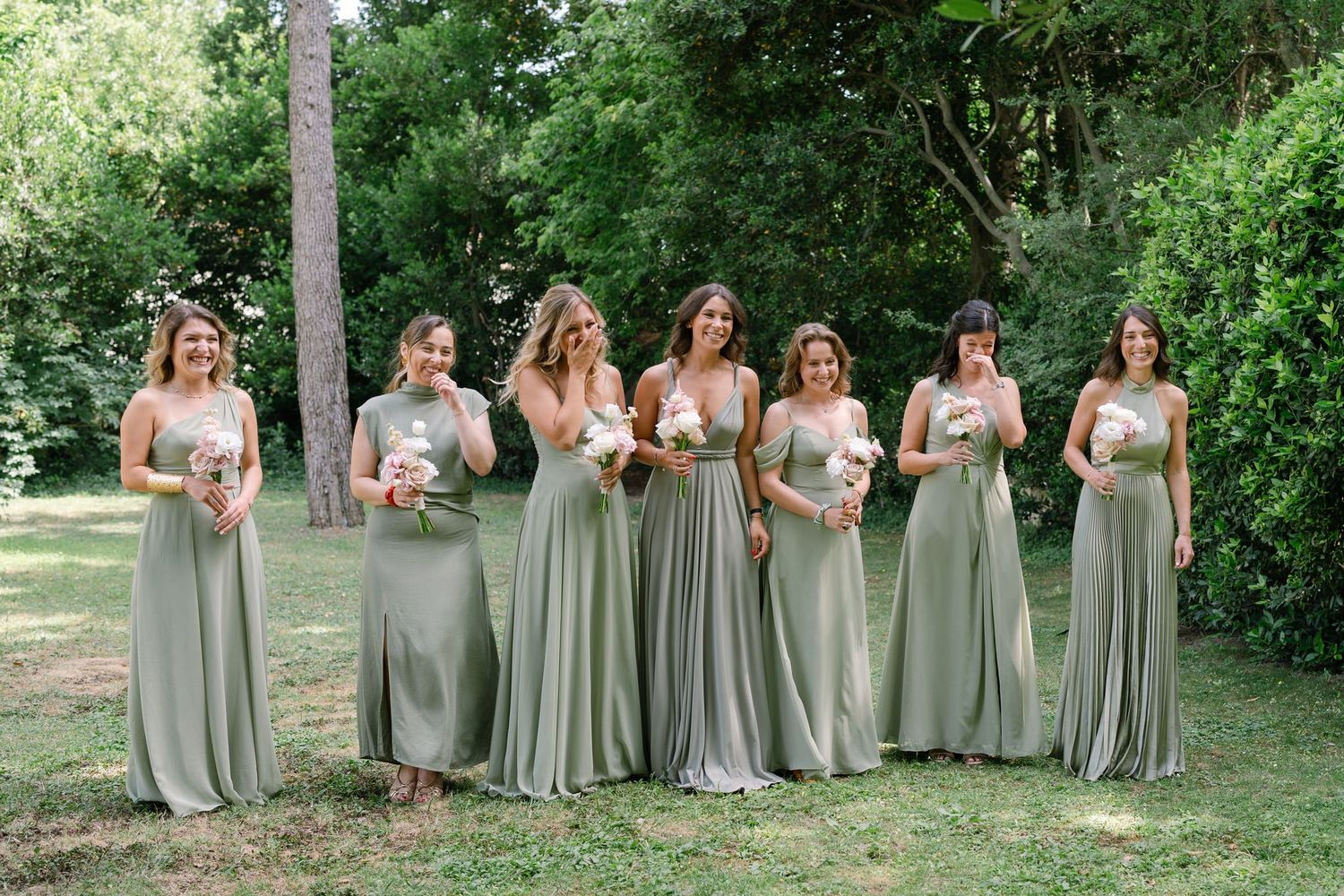 Group photo of bridesmaids wearing sage green dresses and holding pink bouquets in a garden setting.