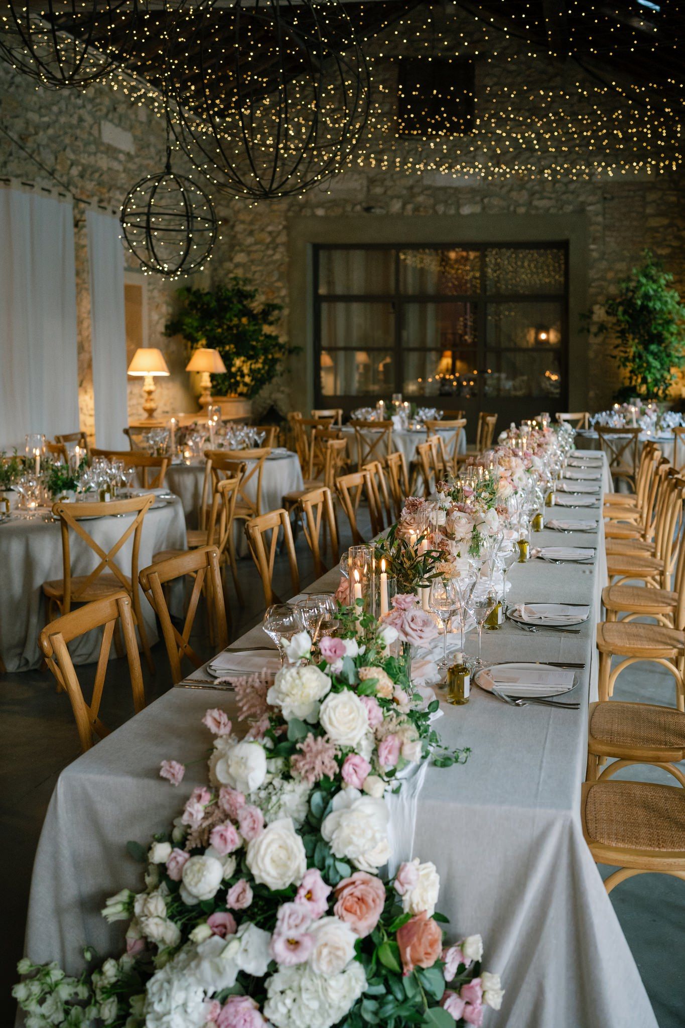 Elegant wedding reception setup with long tables decorated with white linens and string lights overhead.