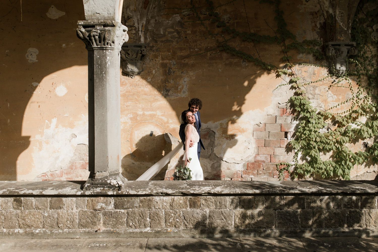 A couple shares an intimate moment beneath historic stone arches and columns.
