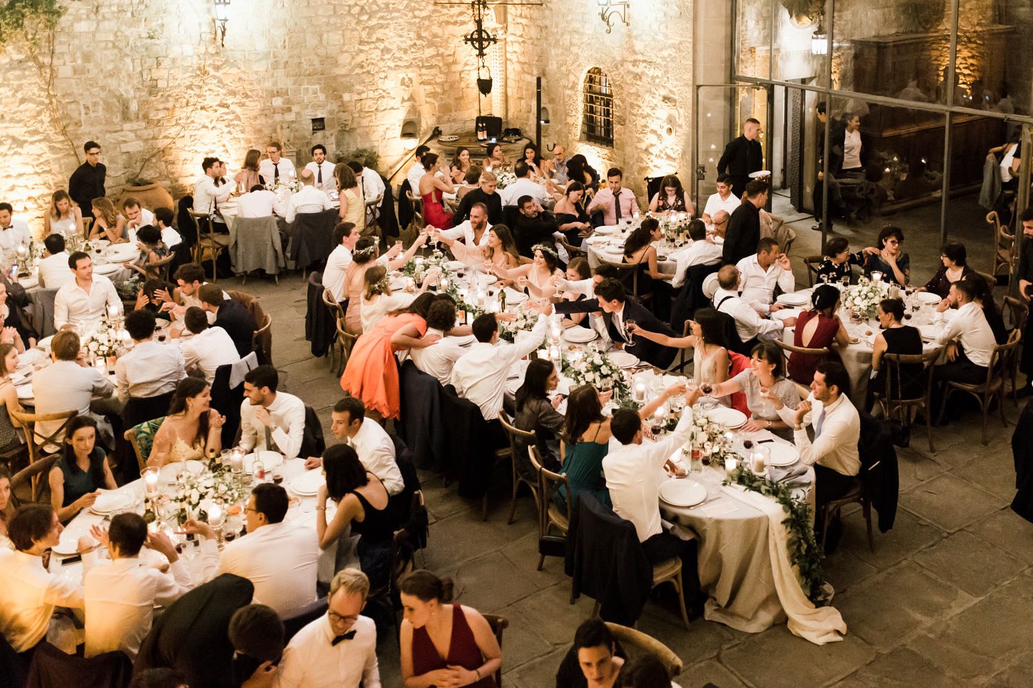 Elegant wedding reception with guests dining at round tables in historic stone venue.