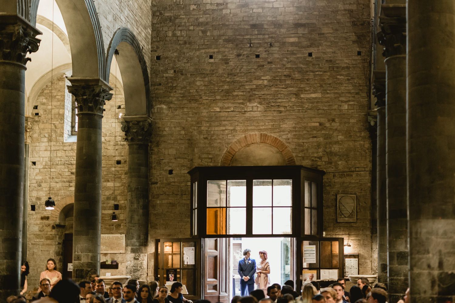 Historic church interior with stone columns and arches filled with wedding guests.