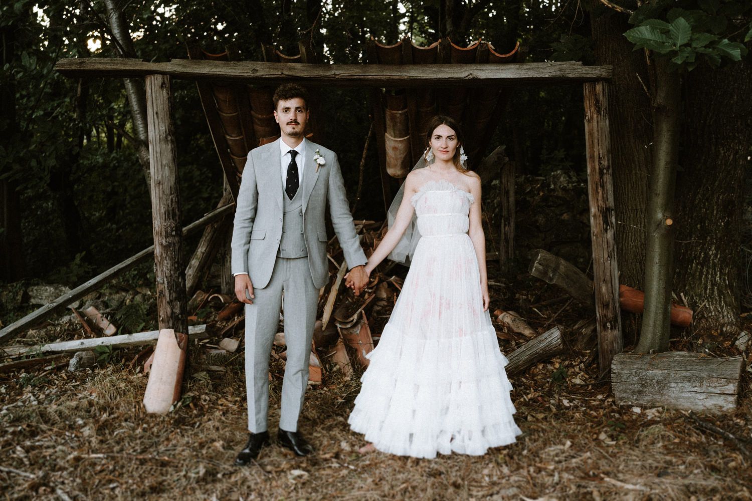 A couple stands together in a rustic outdoor setting for their wedding portraits.