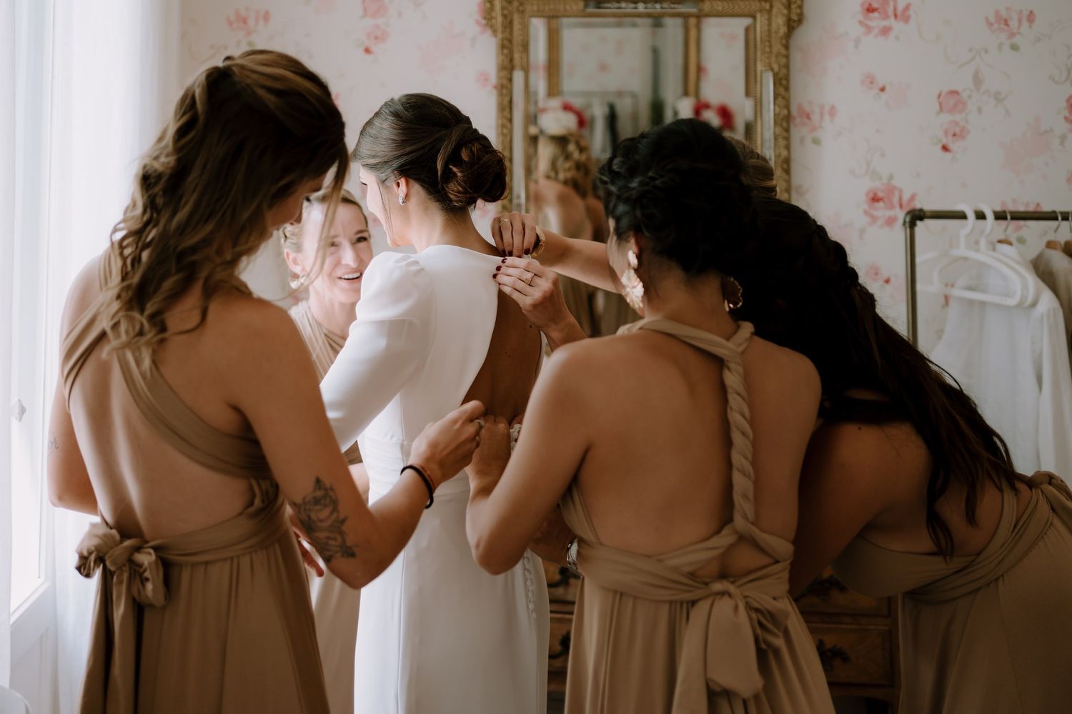 Intimate wedding preparation moment with bridesmaids in neutral dresses helping the bride.