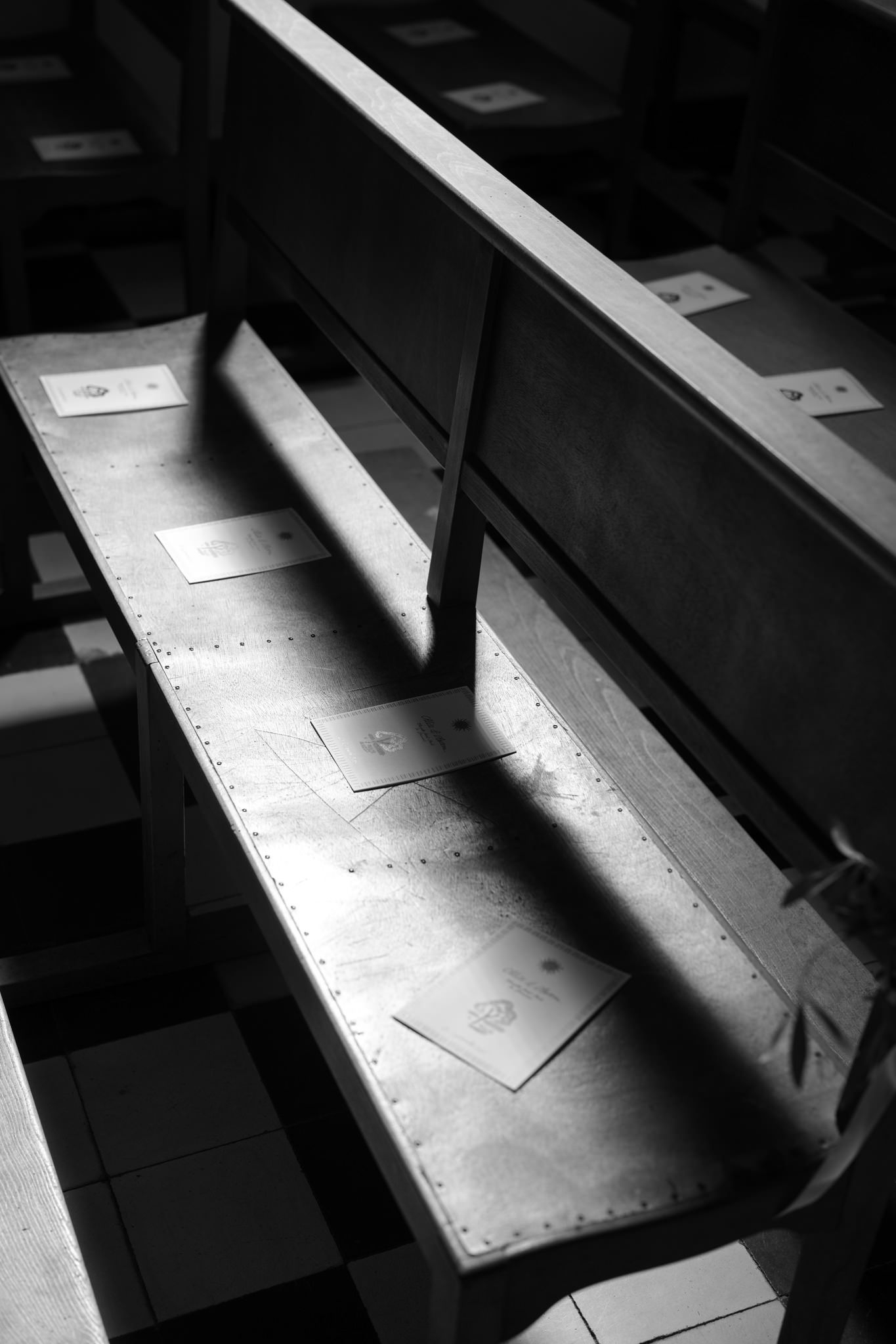 Dramatic black and white image of sunlight casting shadows across wooden church pews.