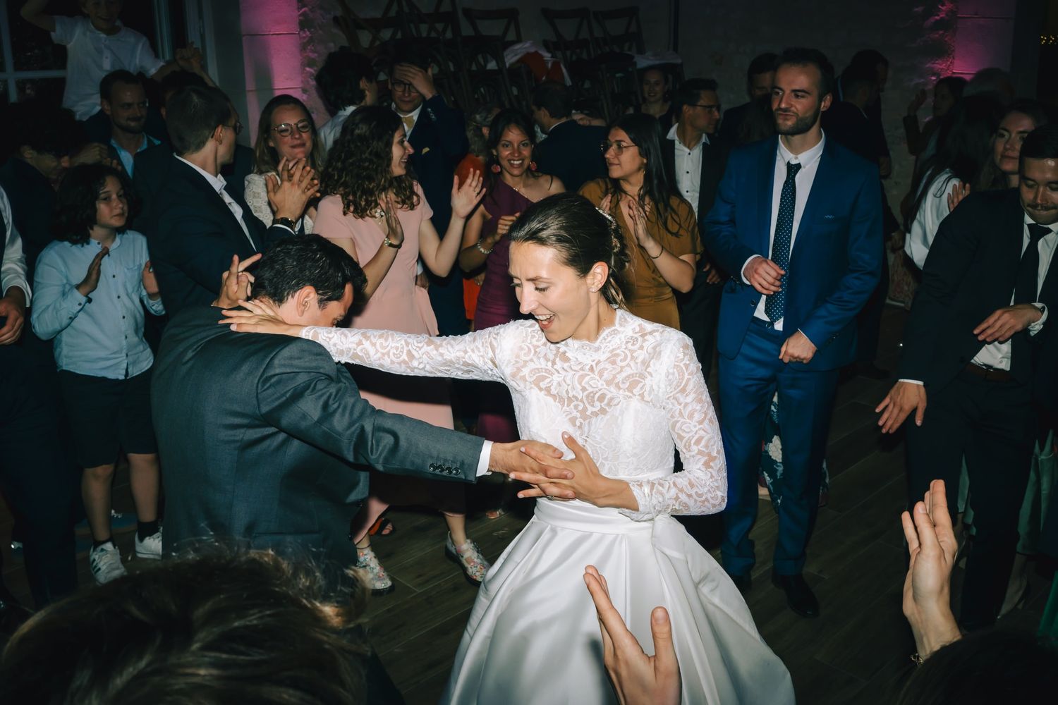 Wedding reception dance floor filled with guests dancing under dim lighting.