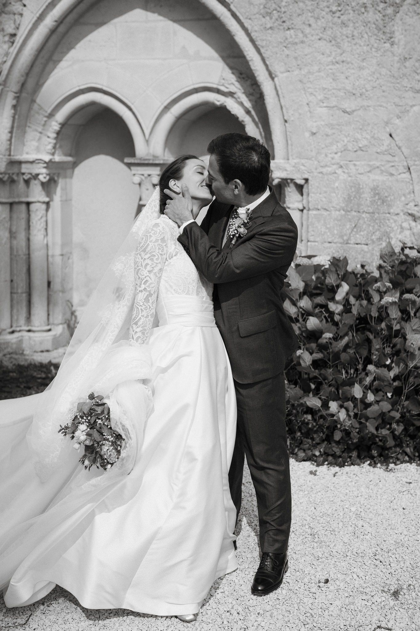 Romantic wedding couple shares intimate moments under stone archways in black and white photography.