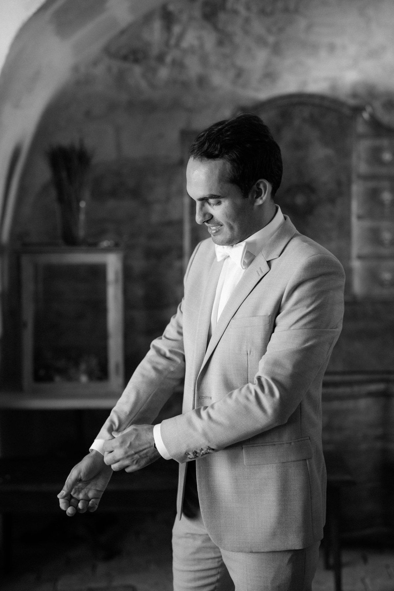 Person in light colored suit adjusting cufflinks in black and white photography.