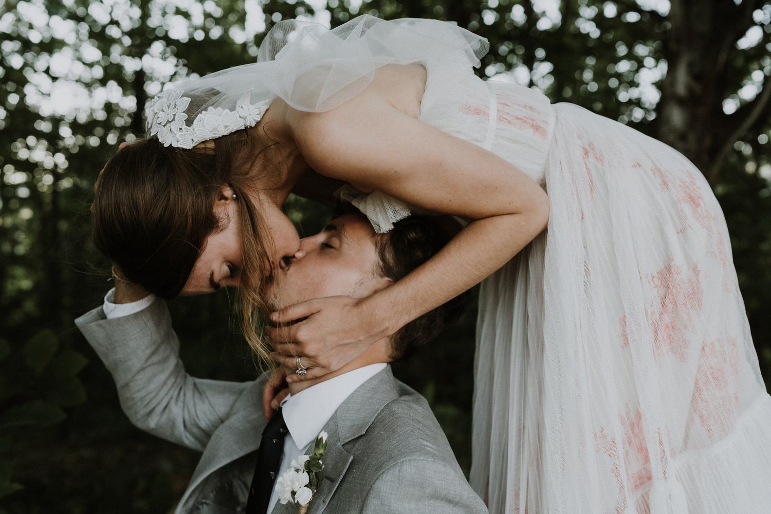 Romantic wedding kiss captured in moody forest setting.