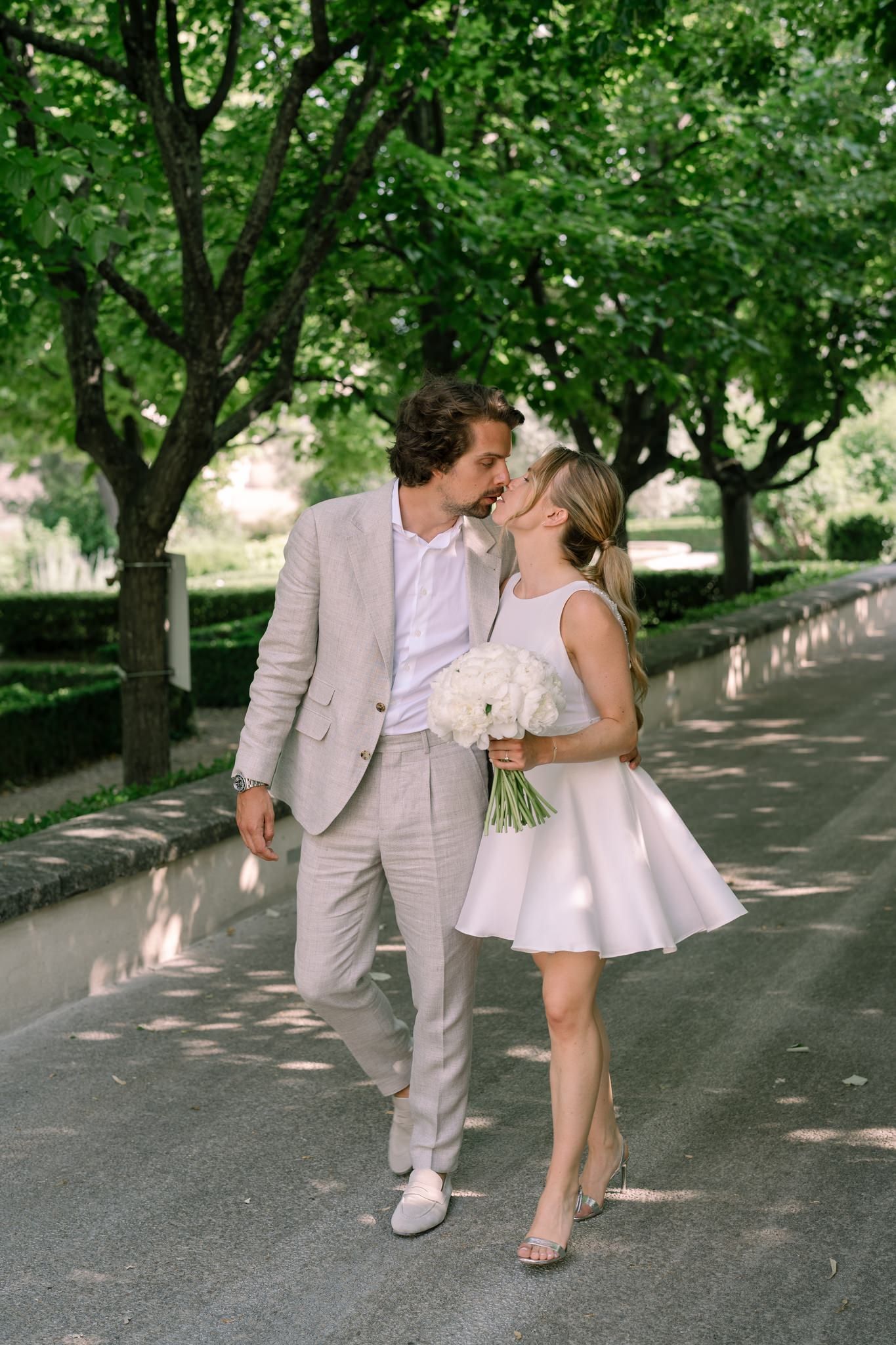 Couple walking playfully under tree-lined path in formal attire.