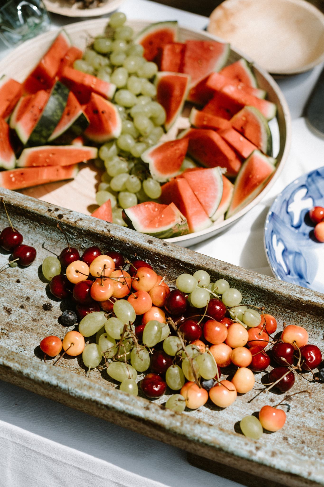 Fresh fruit platter with watermelon slices, green grapes, cherries, and cantaloupe arranged on a rustic tray.