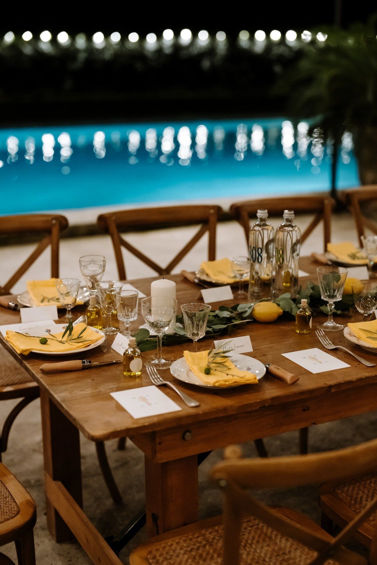 Elegant rustic wedding reception table setup with wooden chairs and string lights overhead.