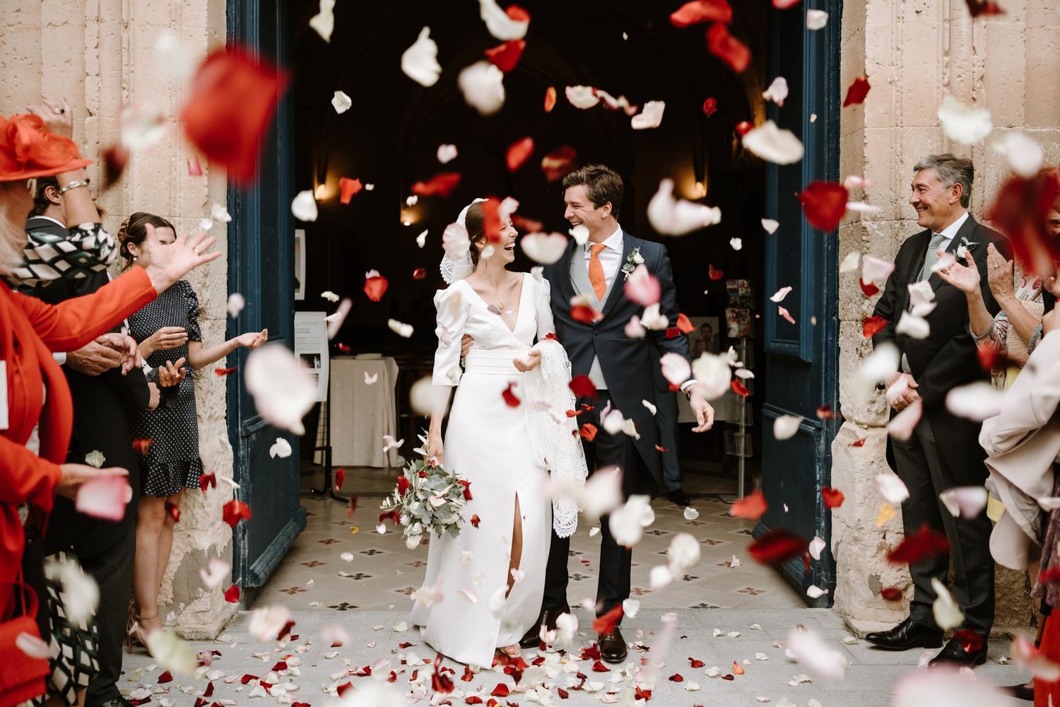 Wedding celebration with red and white confetti being thrown in the air during an outdoor ceremony.