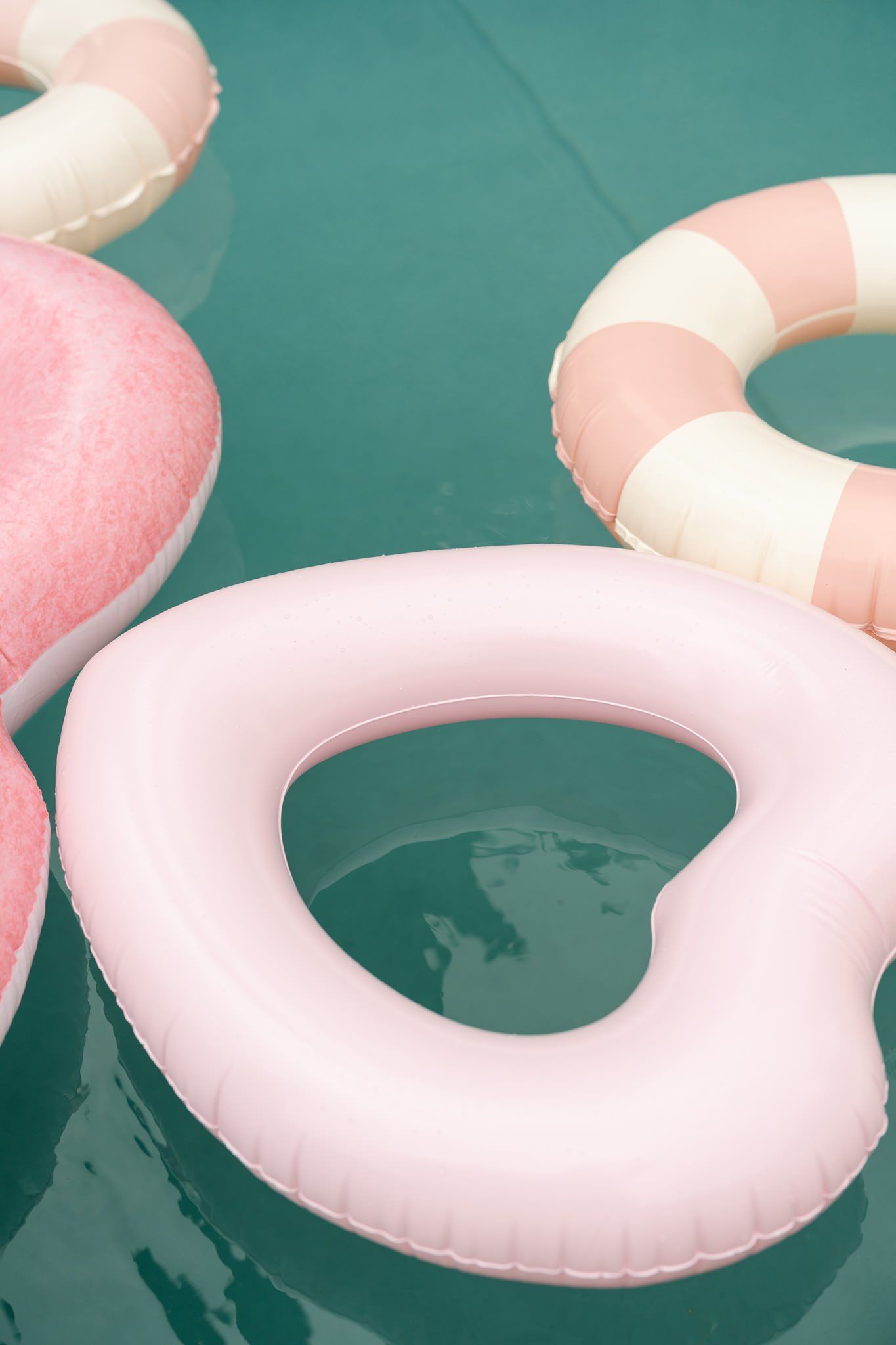 Pink and white pool floats arranged in a row on turquoise water.