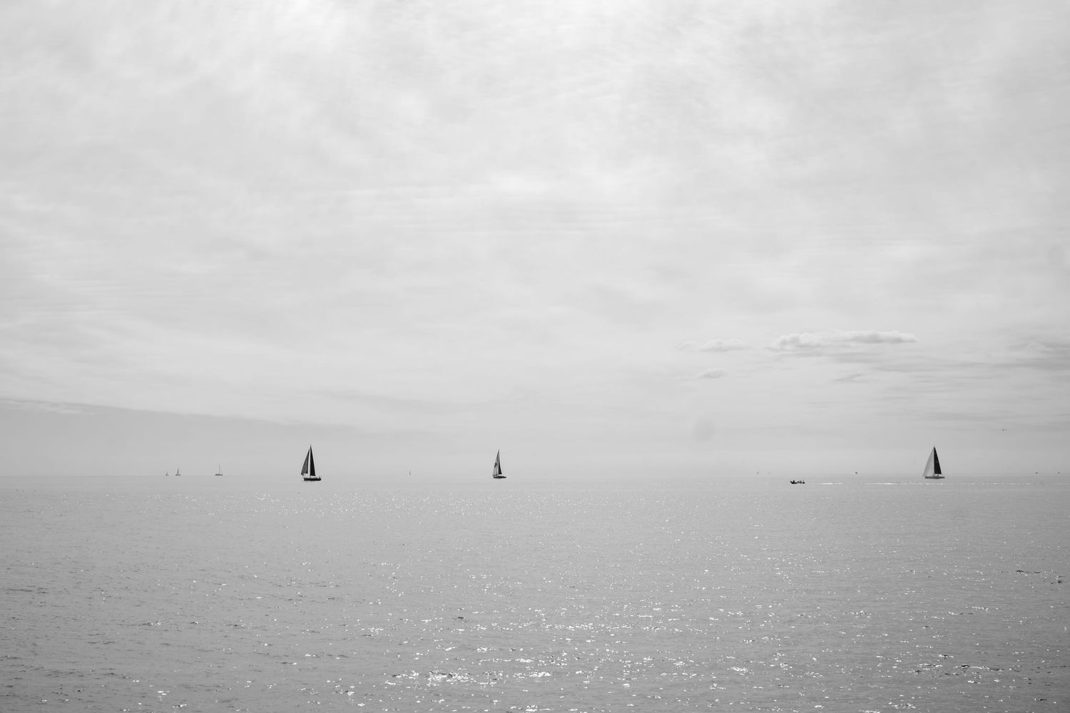 Distant sailboats dot the horizon on a calm ocean under an overcast sky.