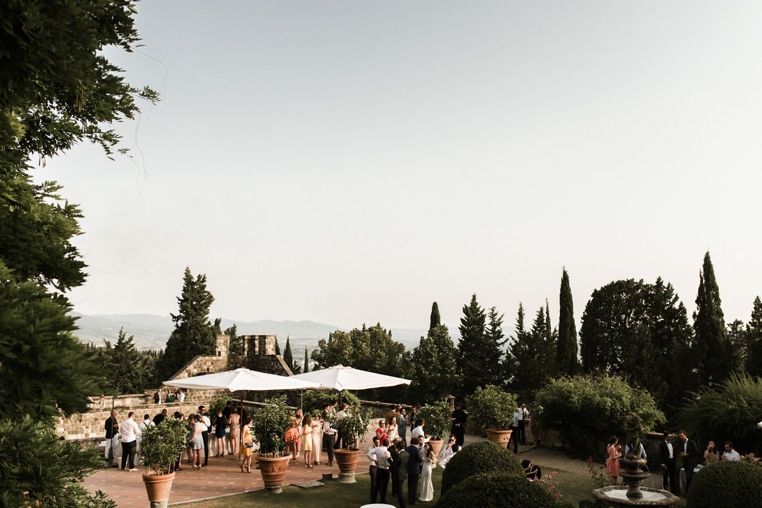 Outdoor wedding reception venue with white tents and tables set up in a lush garden setting at sunset.