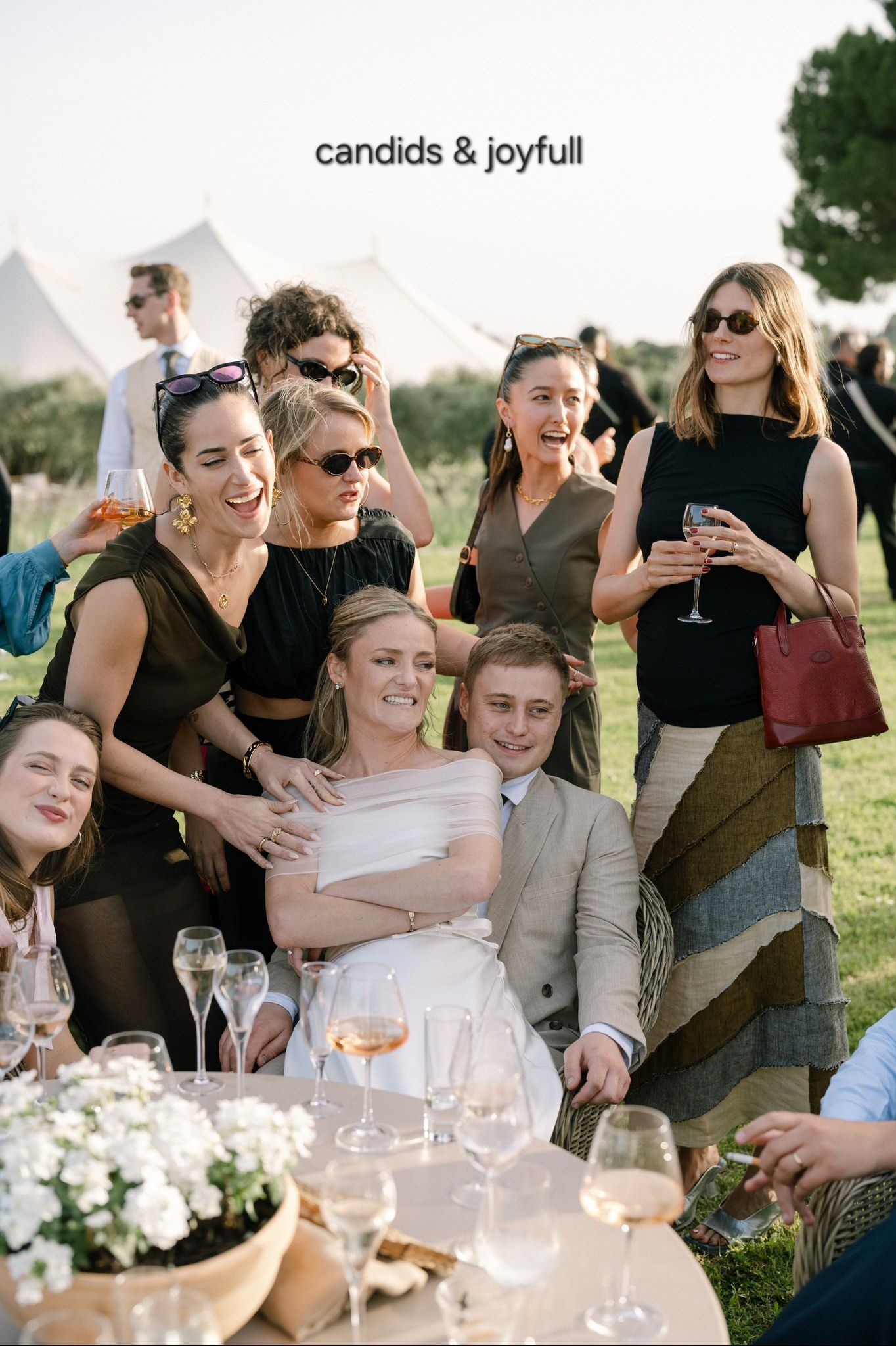 Wedding guests enjoying drinks and conversation at an outdoor reception table with wine glasses.