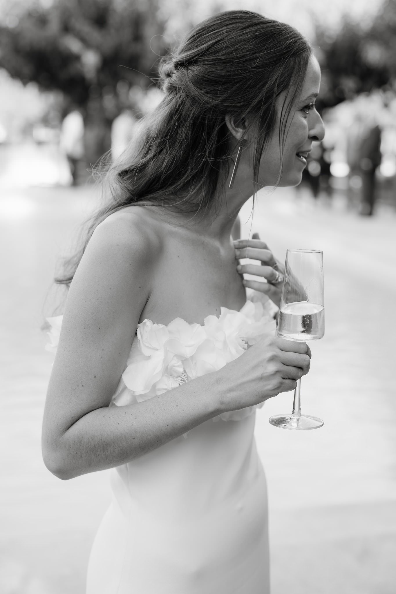Elegant bride in white dress holding champagne glass at outdoor celebration.