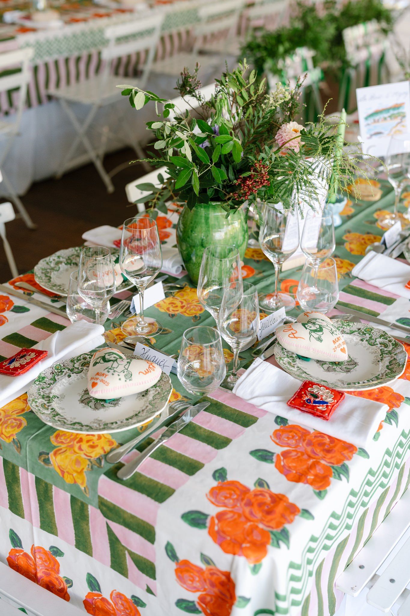 Detailed view of place settings with green and orange floral decor on striped tablecloths.