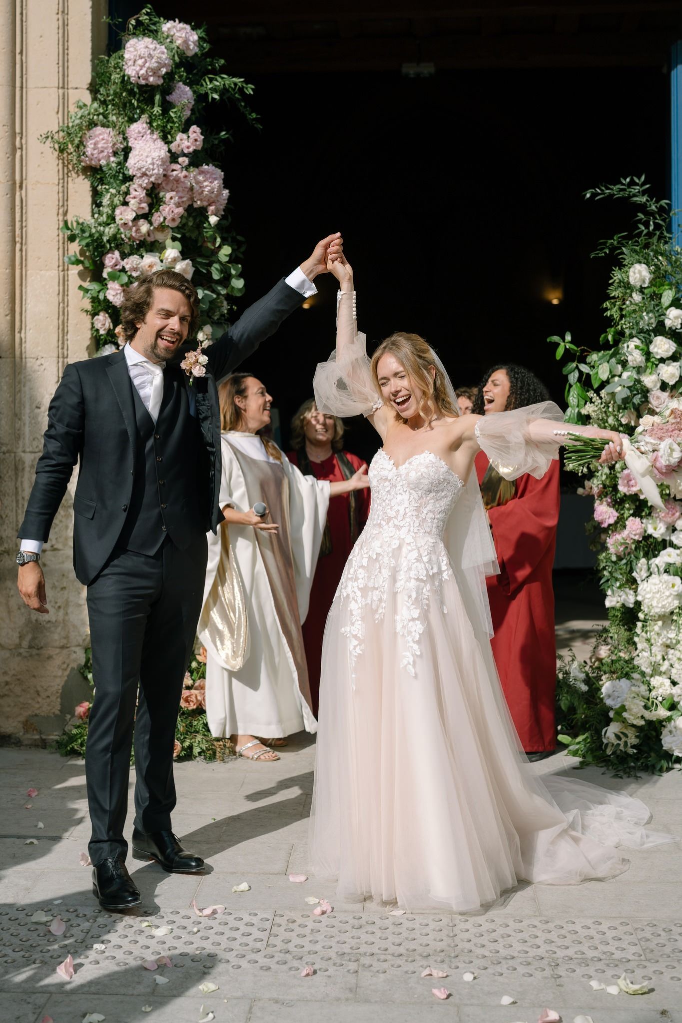 Wedding party celebrating at church entrance decorated with pink and white floral arrangements.
