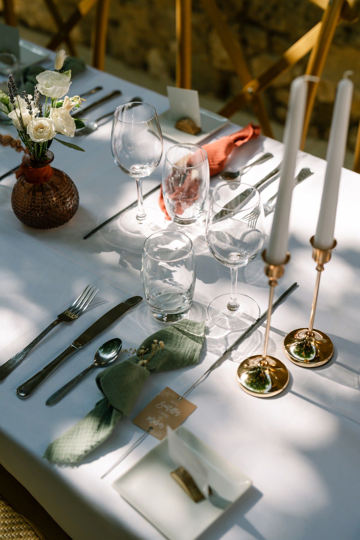Elegant table settings with wine glasses and gold candlesticks in natural sunlight.