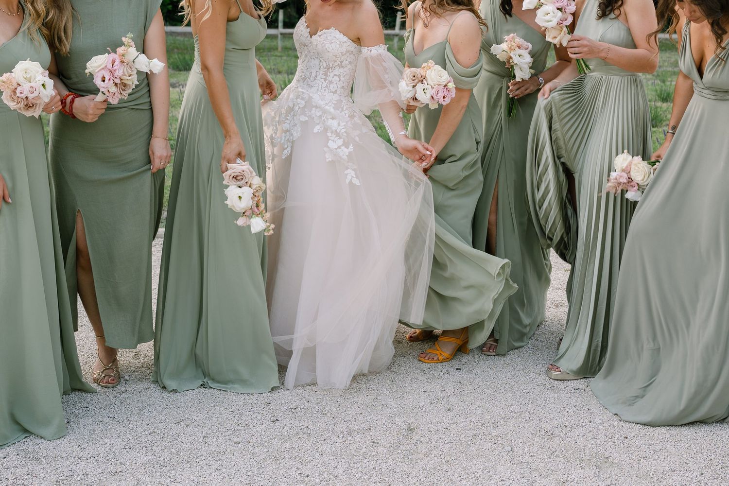Bridesmaids in flowing sage green dresses posing with pink bouquets.