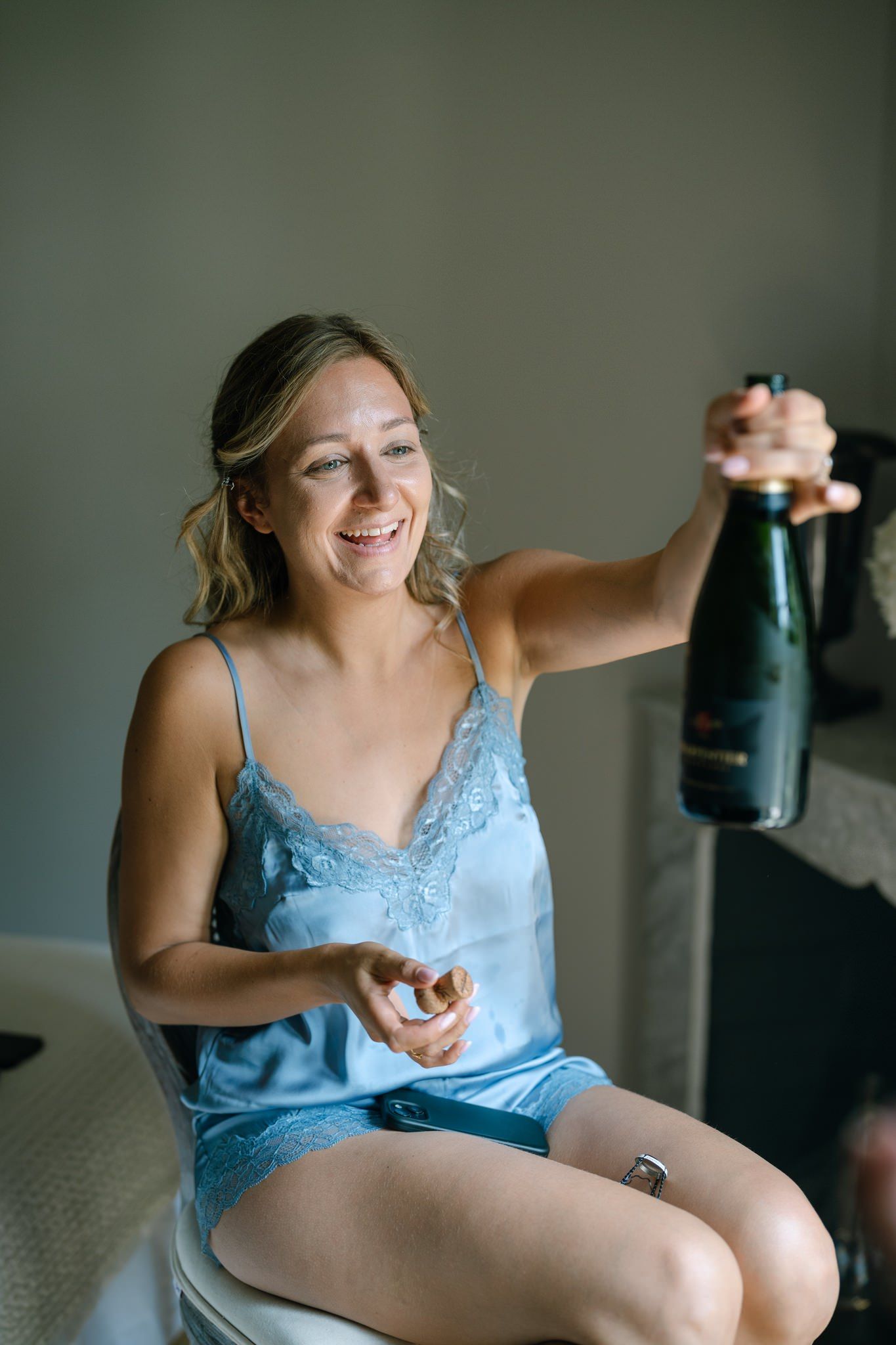 Person in blue loungewear opening champagne during wedding preparations.